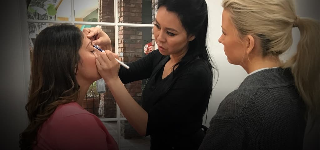 Lindsey Ta mapping a model’s brow shape with a pencil as a student watches during an MLA Academy class