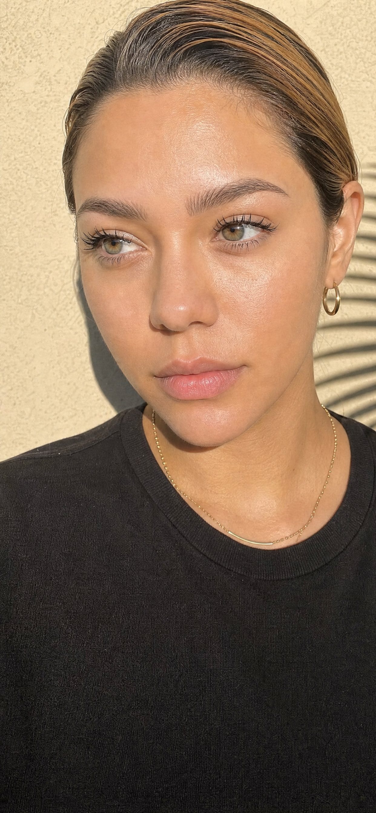Nano Brows client against a sunlit cream stucco wall with a palm shadow