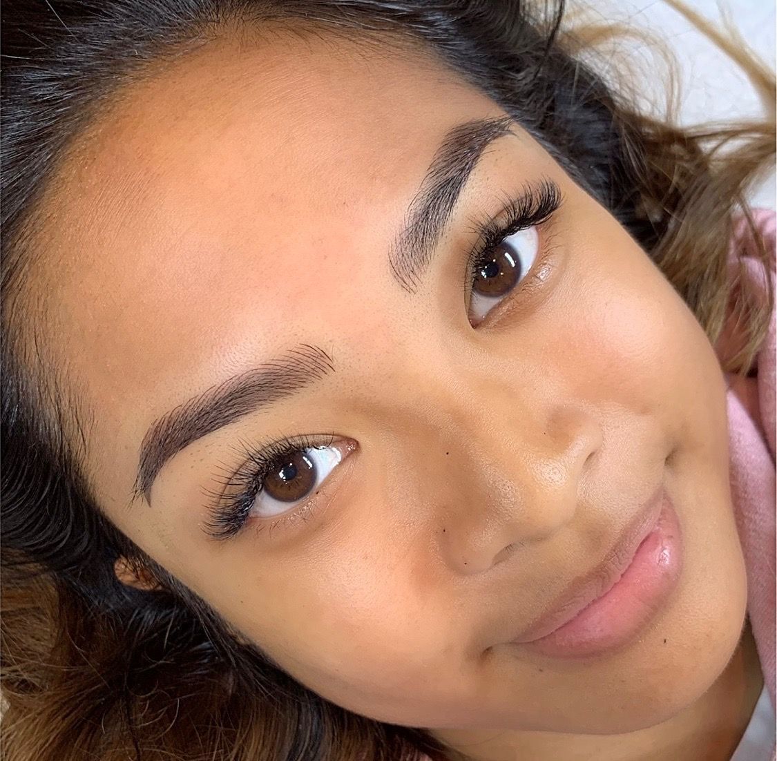 Combo brows results on a smiling woman with dark wavy hair: dark brown brows with a soft, rounded arch, Microblading LA